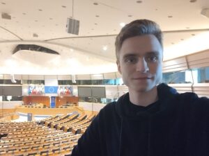 Selfie von Lukas vor dem Plenarsaal des EU-Parlaments in Brüssel. Lukas trägt einen blauen Pullover. Der Plenarsaal ist leer, es ist keine Sitzung